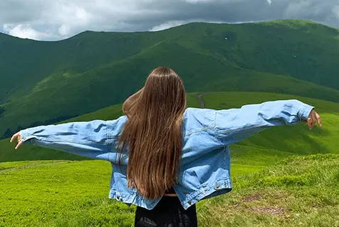 Mujer joven extendiendo los brazos en un campo verde, simbolizando la libertad y bienestar en San Juan de Lurigancho.