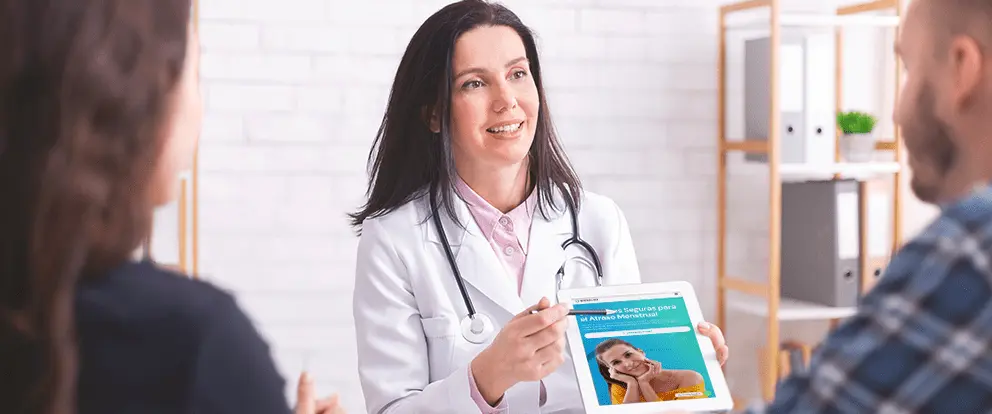 Médico mostrando información en tablet durante consulta sobre solución a atraso menstrual.