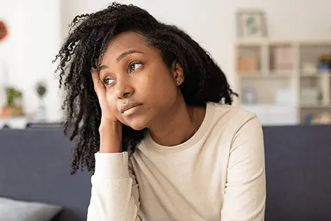 Mujer joven preocupada sentada en casa reflejando ansiedad por atraso menstrual. Solución Rápida.