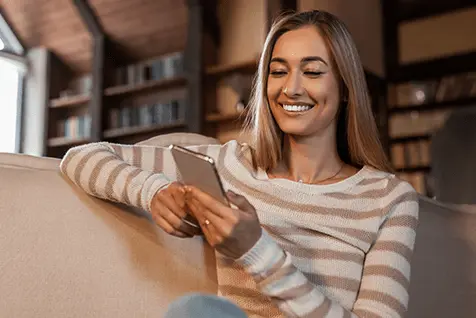 Mujer sonriente en casa leyendo sobre tratamientos para atraso menstrual.